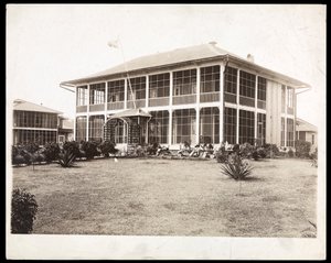 ポーチに囲まれた2階建ての家で、アメリカの旗が飛んでいます。 1912年に運河の建設中にパナマで（銀ゼラチンプリント） 作： Byron Company